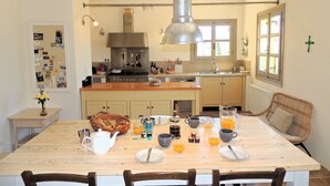 Una cocina con una isla central, sillas de madera, una mesa de comedor dispuesta para el desayuno y una lámpara colgante.