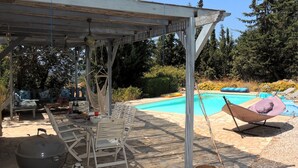 Un espacio al aire libre techado con una parrilla, sillones de descanso y una piscina.