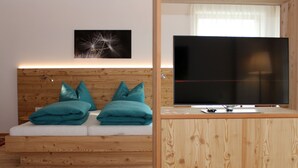 Ein modernes Zimmer mit einem Holz-Kopfteil, türkisfarbenen Kissen, einem Flachbildfernseher und einem an der Wand hängenden Bild.