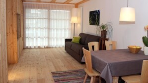 Ein Wohnbereich mit Holzboden, einer Couch, einem Esstisch mit Stühlen, einer Lampe und einem Blumentopf.