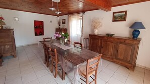 A dining area with a wooden table and chairs, a wooden ceiling, and a cabinet with a lamp. - Maison de Campagne à 50 m de la Rivière Lot (Saint-Martin-Labouval)
