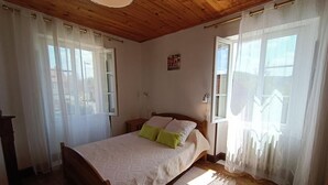 A bedroom with a wooden bed, a nightstand, a lamp, and sheer curtains. - Maison de Campagne à 50 m de la Rivière Lot (Saint-Martin-Labouval)