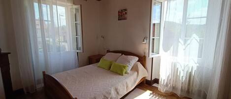 A bedroom with a wooden bed, a nightstand, a lamp, and sheer curtains.