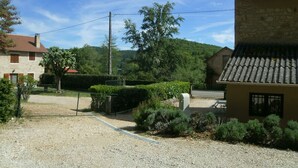 A rural setting with a stone building, a gravel driveway, and a fenced area with greenery. - Maison de Campagne à 50 m de la Rivière Lot (Saint-Martin-Labouval)