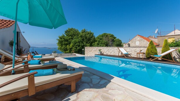 A pool area with lounge chairs and a large umbrella, surrounded by stone walls and greenery.
