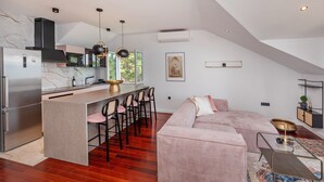 A modern kitchen with a central island, bar stools, and a dining area with a sofa and coffee table.