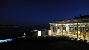 A glass-enclosed building with a dining area, overlooking a body of water at night. - Villa Teodora in Toscolano-maderno (Toscolano Maderno)