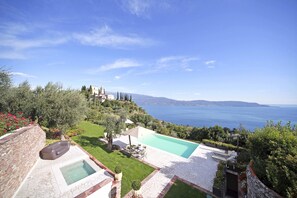 Zona de piscina con vista al mar, rodeada de vegetación y un muro de piedra.
