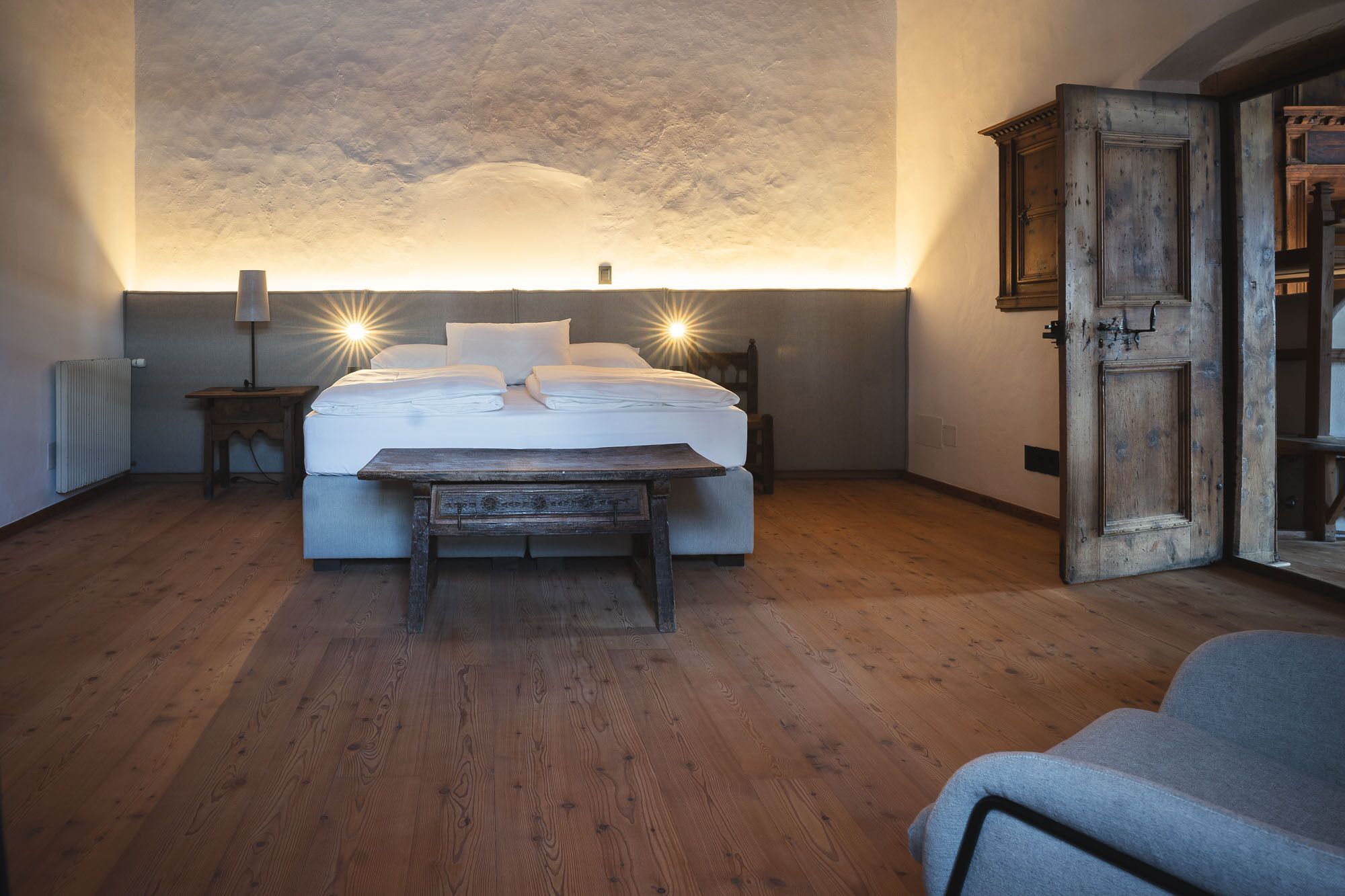 Un dormitorio con una cama grande, un banco de madera, un radiador y una puerta de diseño rústico.