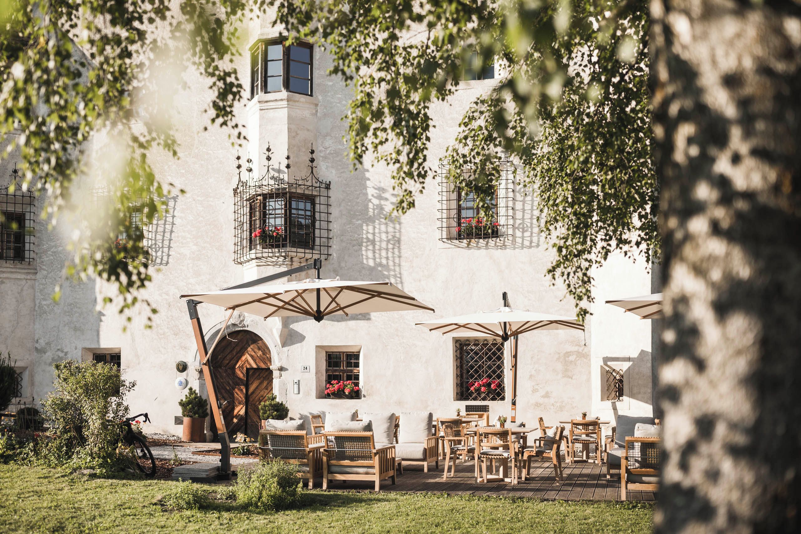 Ein Innenhof mit Außenbestuhlung, einer Holztür und einem Gebäude mit zahlreichen Fenstern und Balkonen.