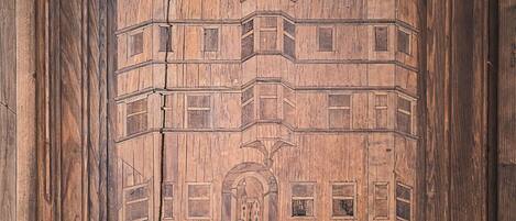 A wooden panel with a carved architectural design, including a building with multiple windows and a central archway.