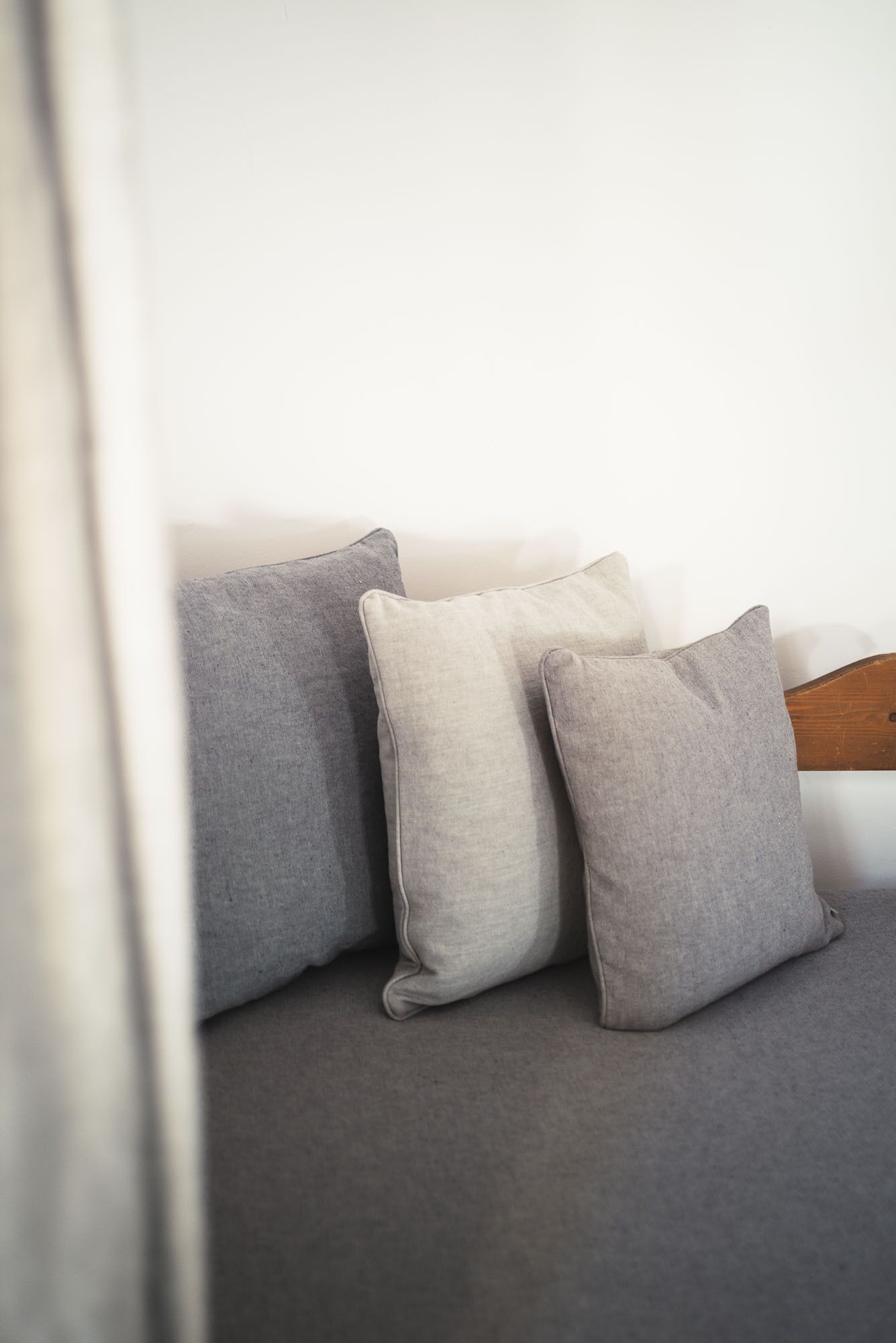 A corner of a room with a grey sofa and three pillows.