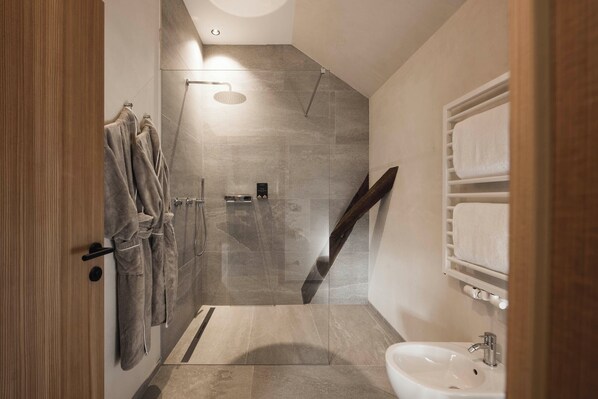 A modern bathroom with a glass shower enclosure, a wooden door, and a white sink.