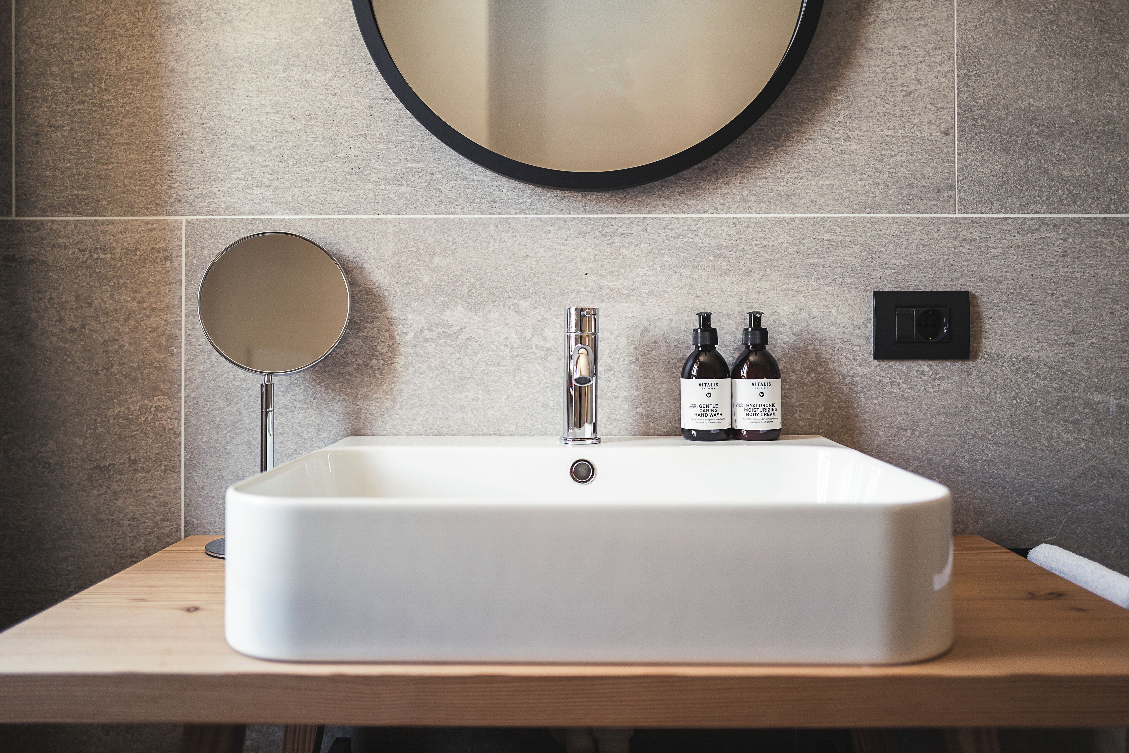 Un baño con un lavamanos rectangular, un espejo redondo y dos botellas de jabón para manos sobre la encimera.