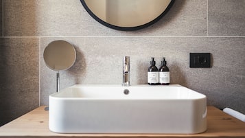 Un baño con un lavamanos rectangular, un espejo redondo y dos botellas de jabón para manos sobre la encimera.