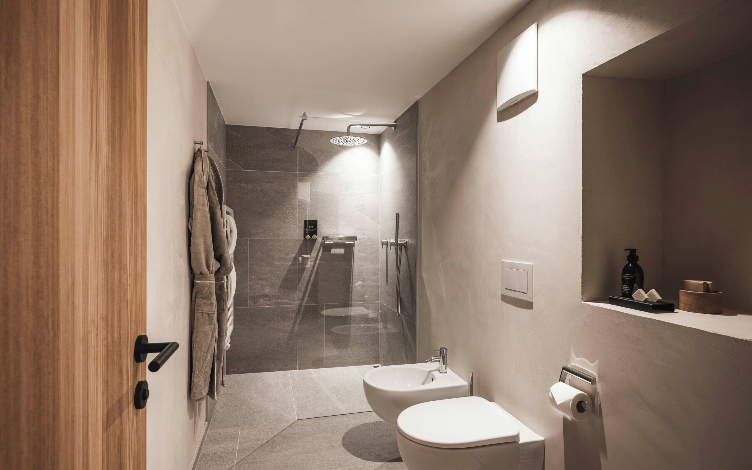 A modern bathroom with a shower, toilet, and bidet. There is a towel rack and a mirror on the wall.