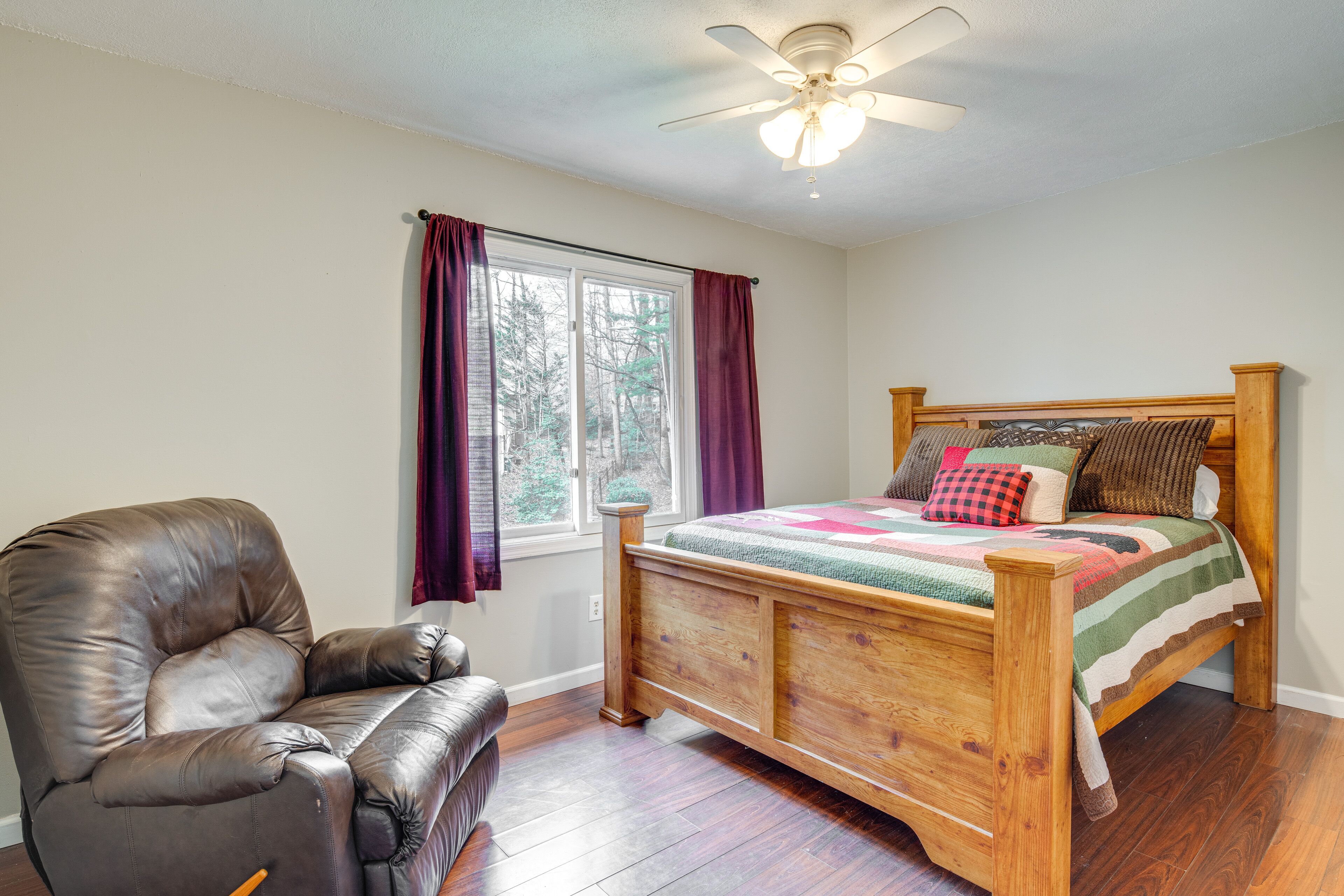 Une chambre à coucher avec un lit en bois, un fauteuil en cuir, une fenêtre avec des rideaux et un ventilateur de plafond.
