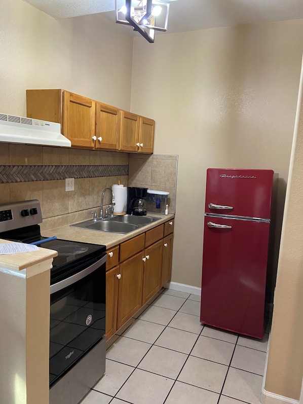 A compact kitchen with wooden cabinets, a stainless steel sink, a red refrigerator, and a black stove.