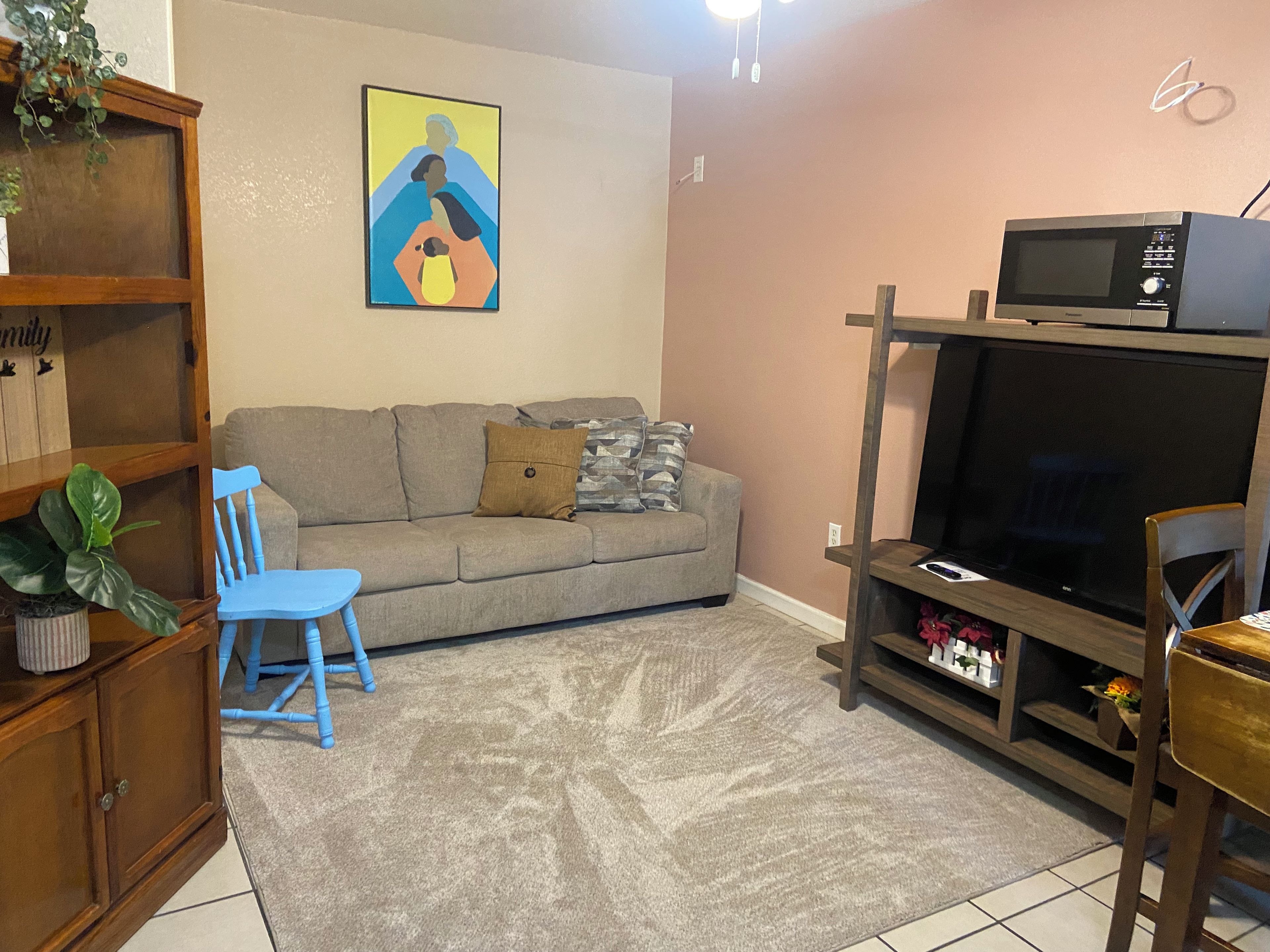 A living room with a sofa, a television on a stand, a blue chair, and a wooden cabinet.