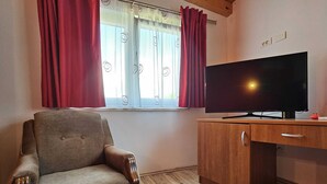Una stanza con una scrivania in legno, una televisione, una poltrona imbottita e una finestra con tende rosse.