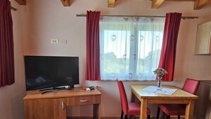 Una stanza con una scrivania in legno, una televisione, un tavolo da pranzo con sedie e una finestra con tende.
