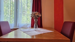 Una mesa de madera con un florero de flores secas, cortinas rojas y una ventana con cortinas blancas y adornos circulares.