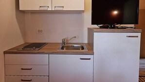 Una kitchenette compacta con pileta, alacenas, una mesada y un televisor de pantalla plana.