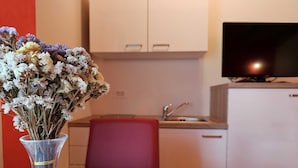 Una cocina con armarios blancos, una silla roja y un florero con flores secas sobre una mesa de madera.