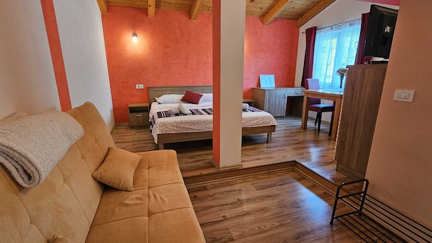 Una habitación acogedora con techo de madera, una cama con almohada roja, un escritorio con silla y un televisor sobre un mueble.
