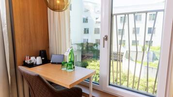 A hotel room with a wooden desk, a laptop, a green bottle, and a coffee machine.