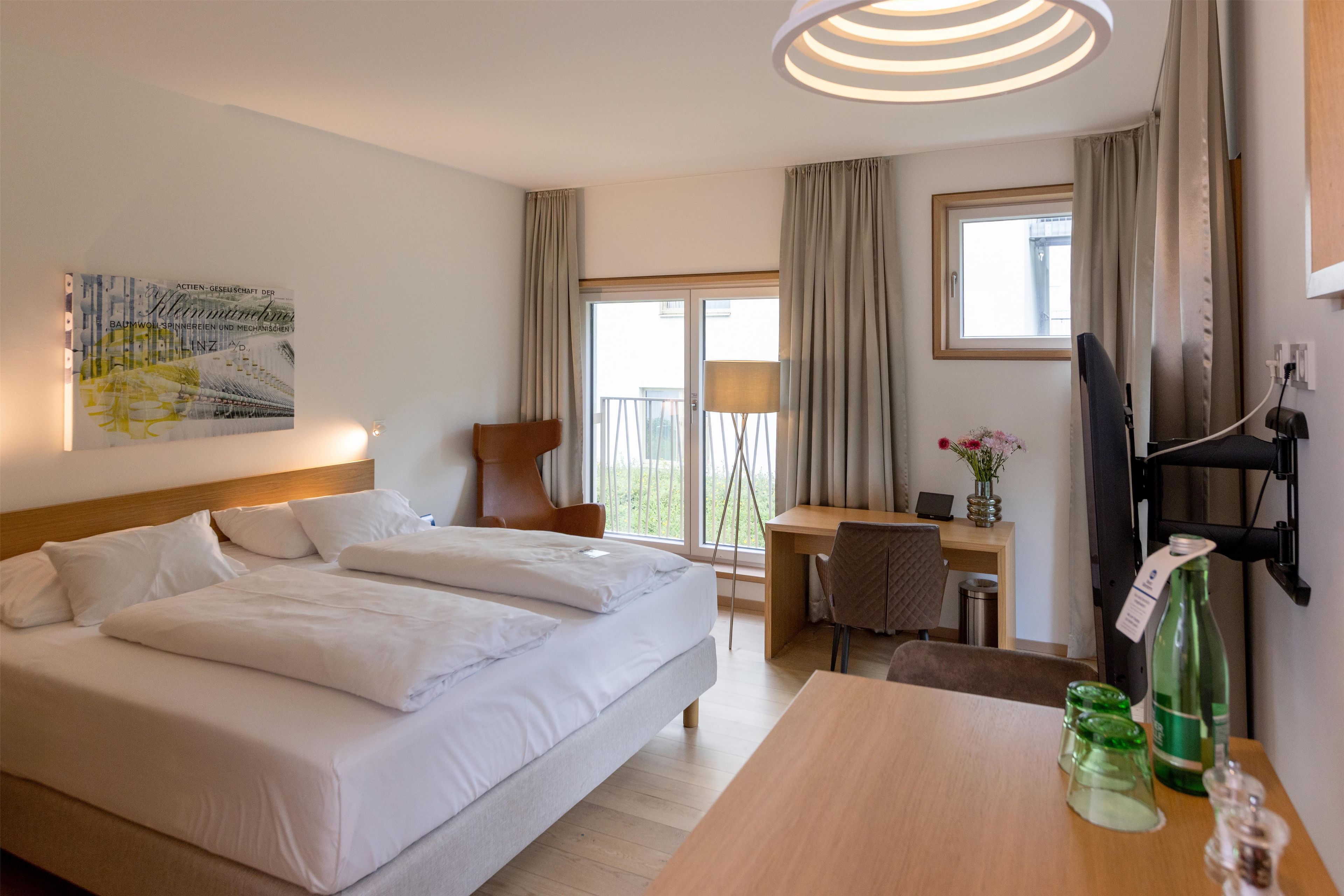 A hotel room with a bed, a desk, a chair, a TV, and a window with curtains.