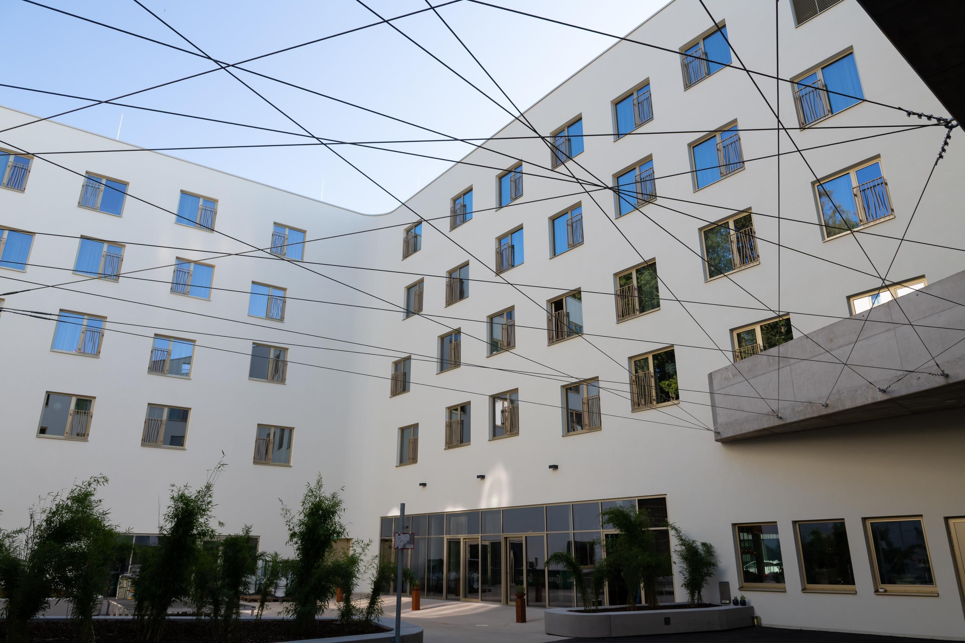 Un immeuble à plusieurs étages doté d’une architecture moderne, avec un patio central agrémenté de plantes en pot et une entrée en verre.