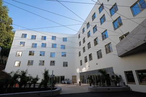 Un edificio moderno con varios pisos, amplias ventanas y un patio con plantas en macetas.