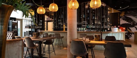 A bar area with hanging wicker lamps, a bar counter with stools, and shelves stocked with bottles.