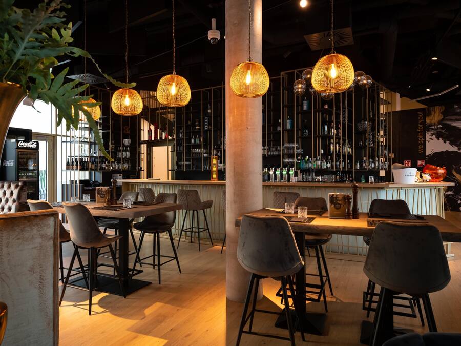 A bar area with hanging wicker lamps, a bar counter with stools, and shelves stocked with bottles.