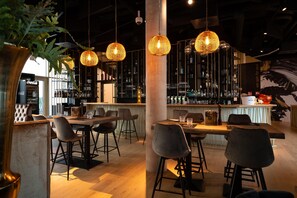 A bar area with hanging wicker lamps, a bar counter with stools, and shelves stocked with bottles. - Best Western Hotel Spinnerei Linz (Linz)