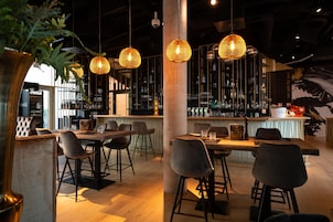 A bar area with hanging wicker lamps, a bar counter with stools, and shelves stocked with bottles.