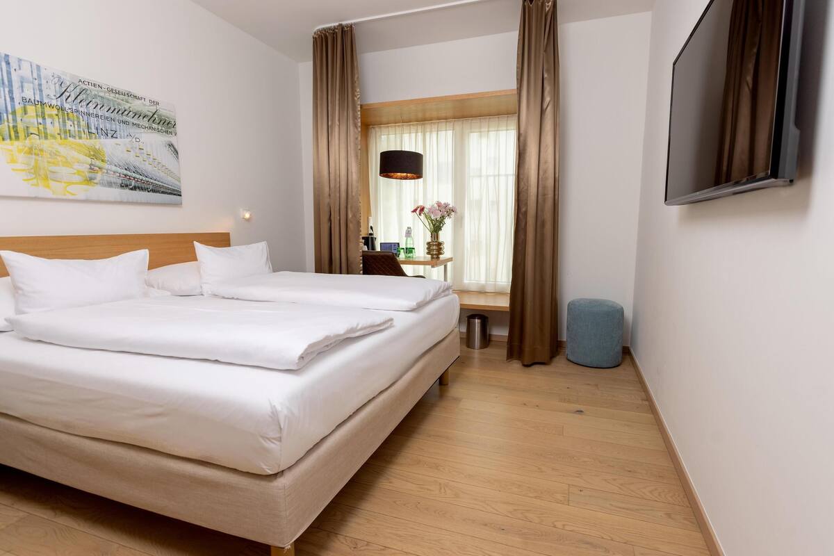 A hotel room with a large bed, a desk with a lamp, and a TV on the wall.