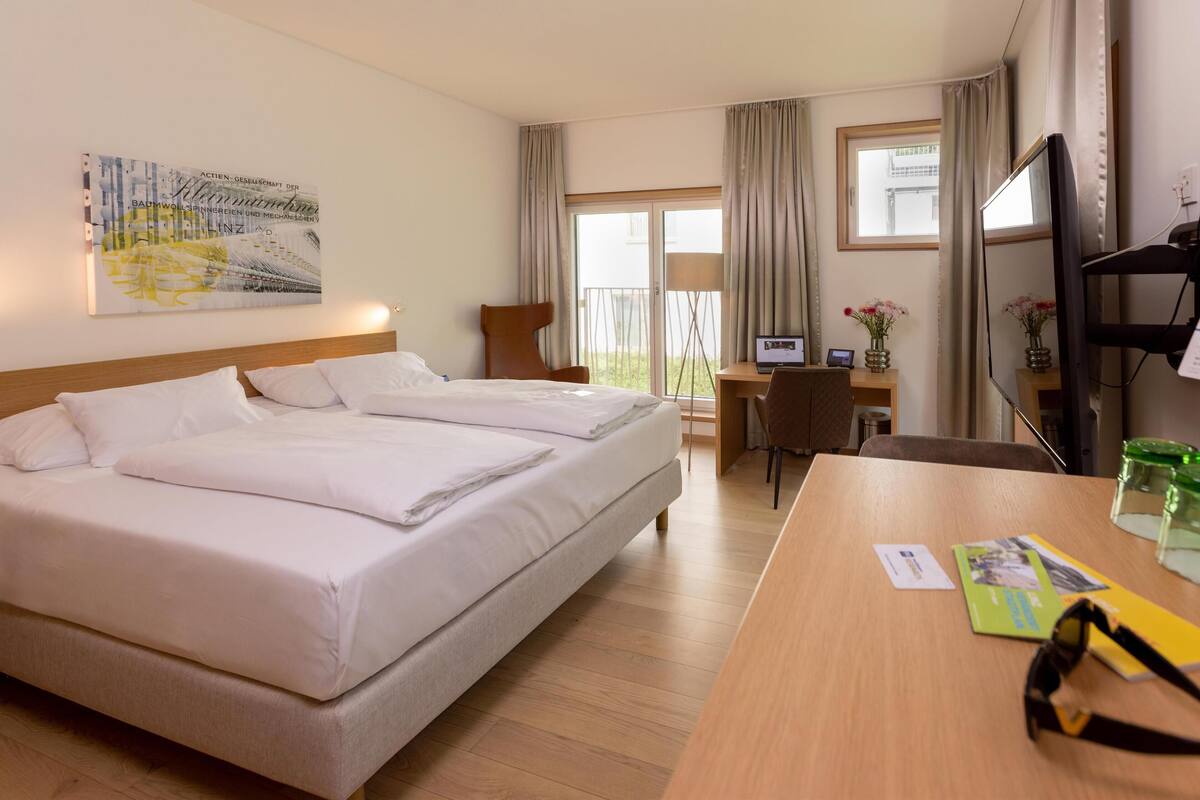 A hotel room with a double bed, a desk with a computer, a chair, and a TV.