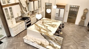 A modern kitchen with marble countertops, white cabinetry, and a herringbone-patterned floor.