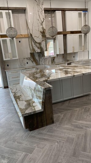 A modern kitchen with marble countertops, wooden cabinets, and herringbone-patterned flooring.