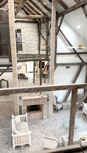 A spacious loft with exposed wooden beams, a stone fireplace, and a herringbone-patterned floor.