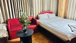 Habitación de hotel con sofá rojo, una mesita redonda con una planta, cama con ropa de cama blanca y paneles de madera en las paredes.