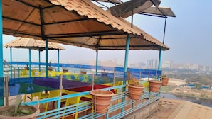 Una terraza con vistas a un paisaje urbano, que incluye una barandilla de metal, sillas de plástico de colores y macetas de terracota.