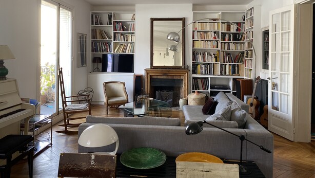 Tilava olohuone, jossa on suuri kirjahylly, takka ja piano.