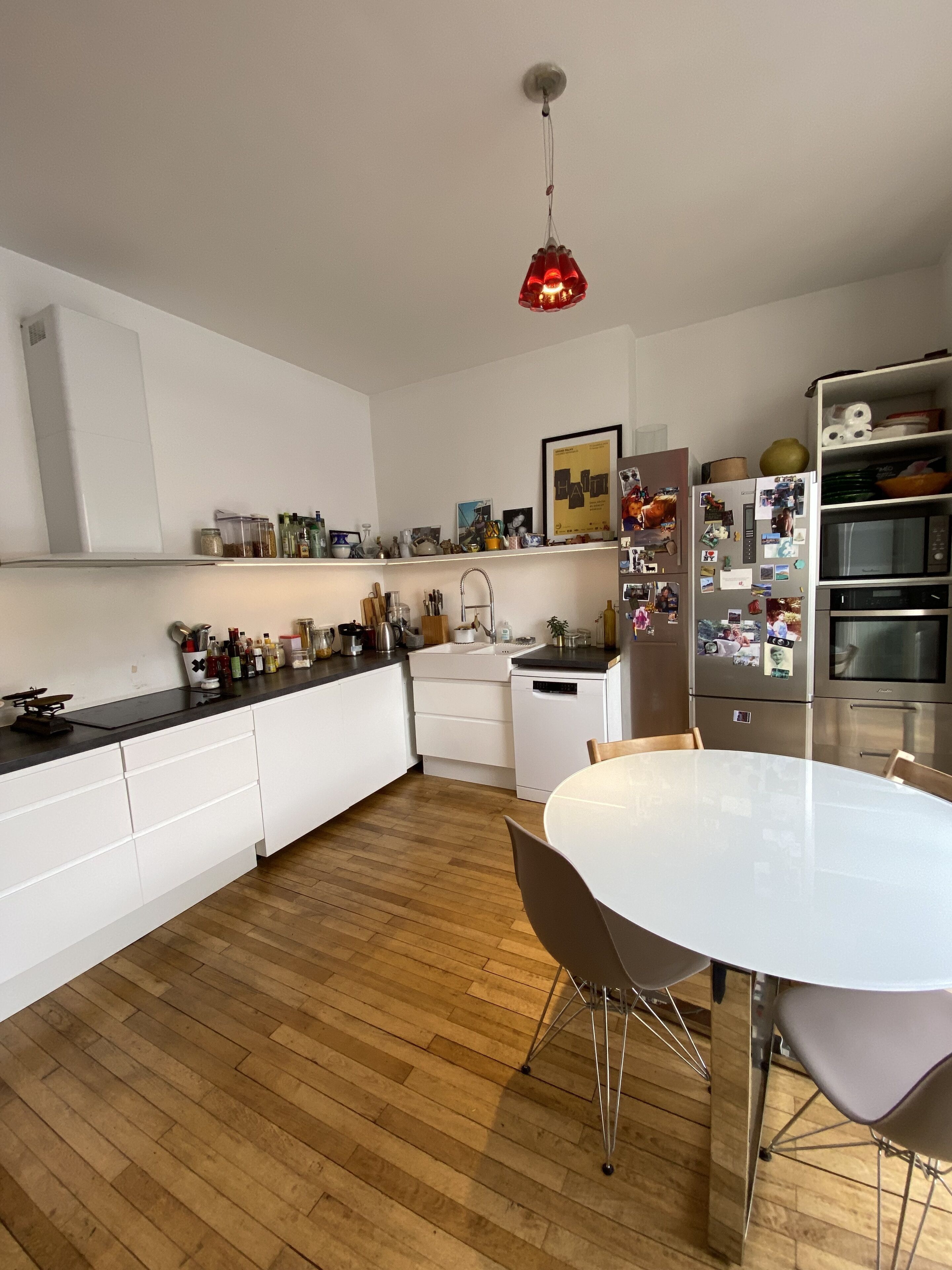 A modern kitchen with white cabinetry, a wooden floor, a dining table with chairs, and a hanging pendant light.