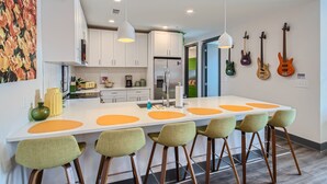 A modern kitchen with white cabinets, a central island with bar stools, and guitars on the wall.