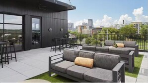 A modern outdoor seating area with a sofa and chairs, a dining table, and a view of the cityscape.