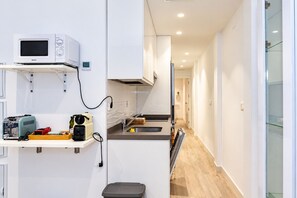 A compact kitchen with a microwave, toaster, and coffee maker on a counter, a small sink, and a wooden floor.