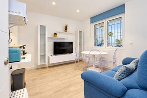 A modern living room with a flat-screen TV, a dining table with chairs, a sofa, and a window with a view of palm trees. - Cubo's Apartment Front Line Beach Fuengirola / First line of beach / Air conditioning (Fuengirola)